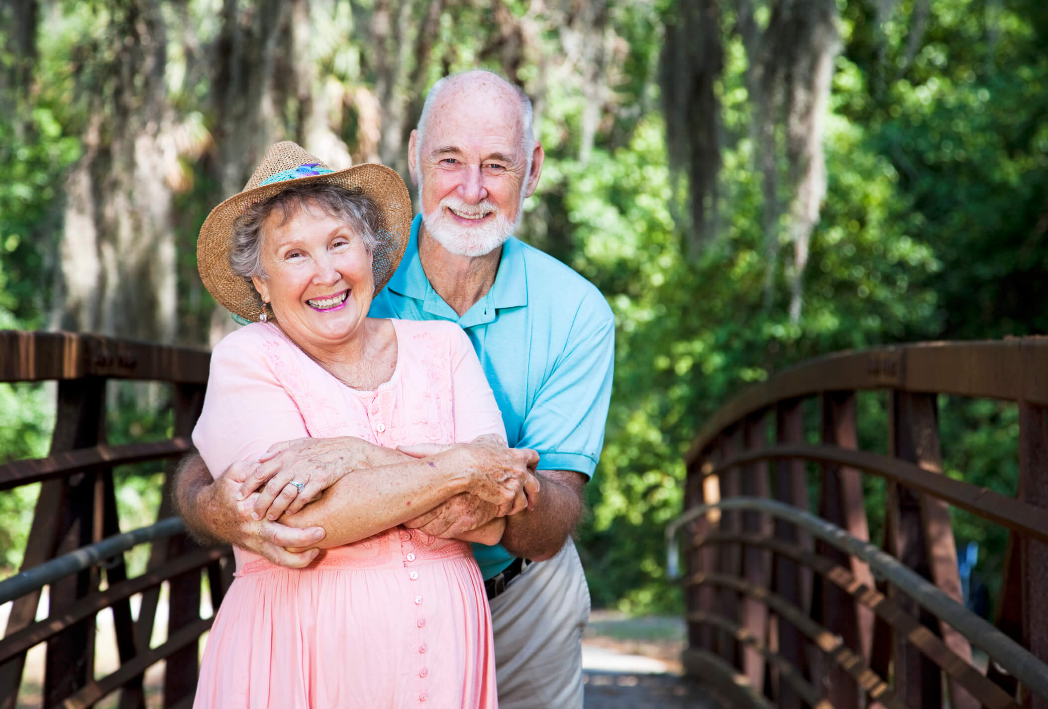 A smiling couple shares an affectionate moment on a wooded bridge, embodying the active, vibrant lifestyle of senior living in Citrus Park, FL near Carrollwood.