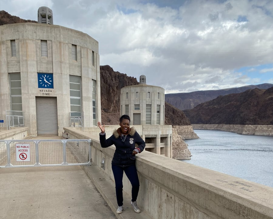 A staff member waves cheerfully while posing in front of a large dam and reservoir — highlighting the passionate team behind senior living Lakeway Texas at Arbor Terrace.