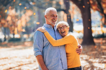 Two older adults laugh and embrace joyfully outdoors among autumn foliage, reflecting the warm, fulfilling lifestyle and meaningful connections found in senior living near Morris Plains, NJ.