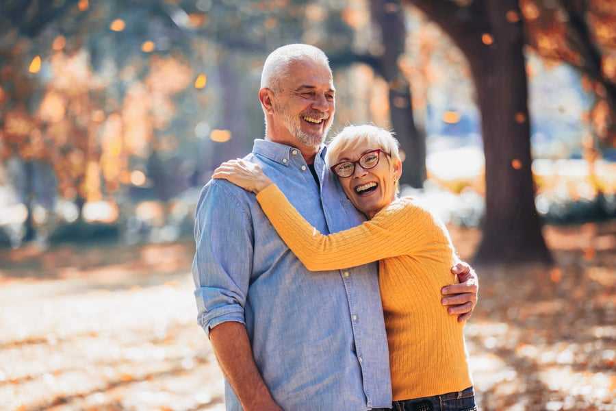 Two older adults laugh and embrace joyfully outdoors among autumn foliage, reflecting the warm, fulfilling lifestyle and meaningful connections found in senior living near Morris Plains, NJ.