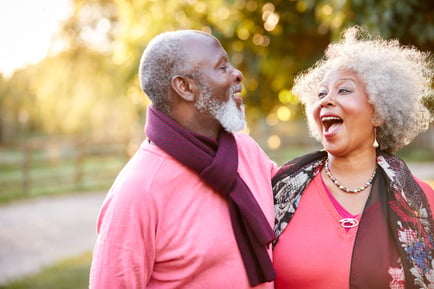 Two older adults share a joyful, lighthearted laugh outdoors on a warm, golden afternoon, embodying the vibrant and fulfilling independent senior lifestyle Herndon VA offers at Arbor Terrace Herndon, a premier active senior living Herndon VA community.