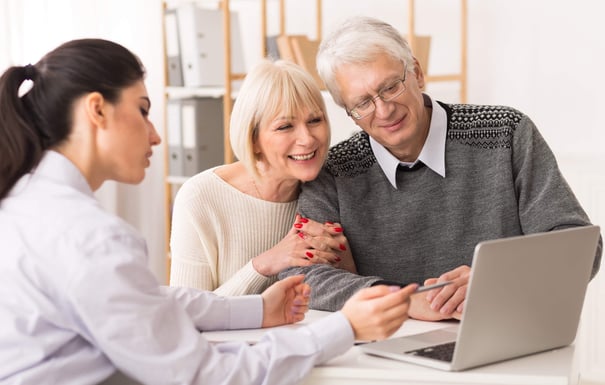 Two older adults smile warmly while reviewing information on a laptop with a staff member, reflecting the personalized, supportive experience of exploring independent living Herndon VA and senior care options Fairfax County at Arbor Terrace Herndon.