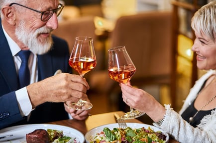 Two older adults clink wine glasses over a candlelit dinner, savoring a refined dining experience at Arbor Terrace Herndon — where senior living with dining and activities Herndon VA meets the independent senior lifestyle Herndon VA residents enjoy.