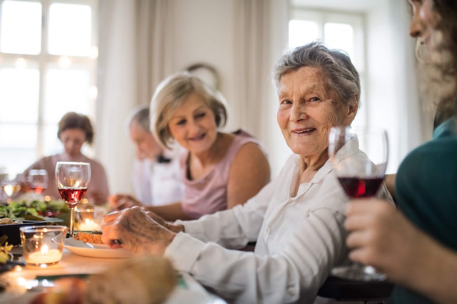 A group of people enjoy a warm, candlelit dinner together, smiling and raising glasses at a vibrant retirement living community in Suwanee, GA