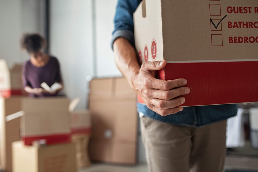 A person carries a labeled moving box while another unpacks nearby, capturing the exciting transition of moving into an assisted living community in Suwanee, GA.