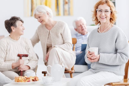 A group of people relax together over tea in a bright, comfortable common area, enjoying warm conversation and community at a senior living community in Suwanee, GA.