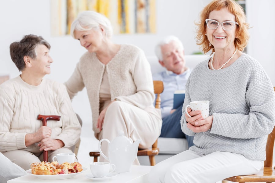 A group of people relax together over tea in a bright, comfortable common area, enjoying warm conversation and community at a senior living community in Suwanee, GA.