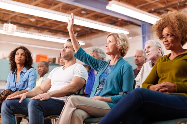 A diverse group of people sit together at a community event, with one person raising their hand to participate, reflecting the engaging programs at senior living in Suwanee, GA.