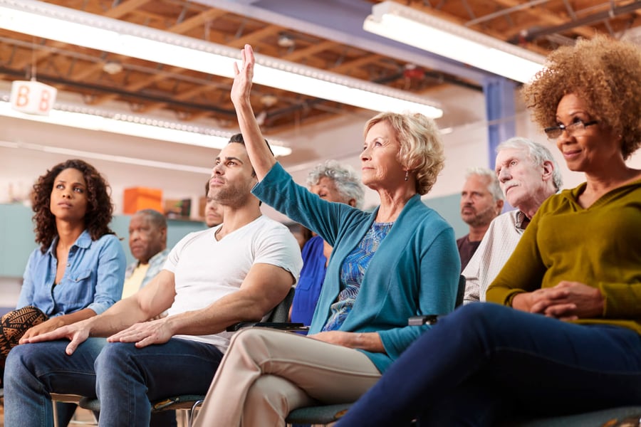 A diverse group of people sit together at a community event, with one person raising their hand to participate, reflecting the engaging programs at senior living in Suwanee, GA.