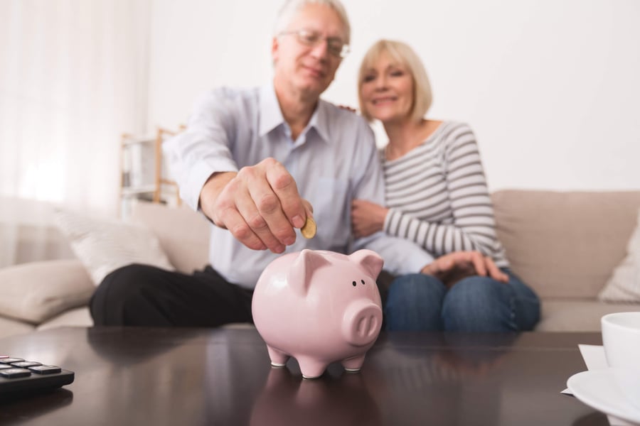 Two people smile together as one drops a coin into a piggy bank, illustrating the transparent, affordable assisted living costs in Suwanee, GA.