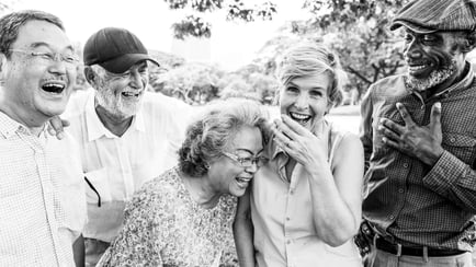 A diverse group of older adults laughs together outdoors in a black and white photo, capturing the joyful friendships that define the active senior lifestyle at a senior living Mount Laurel NJ community.