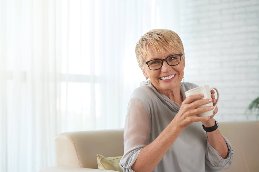 Senior resident on a couch holding a mug smiling 