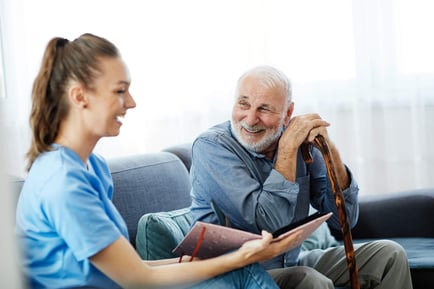A staff member in blue scrubs smiles warmly with an older adult holding a cane — the kind of caring connection found when choosing assisted living near Bee Cave TX.