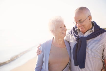 A smiling couple walks together along a sun-drenched shoreline, capturing the vibrant, active lifestyle near senior living near beaches in Clearwater, FL.