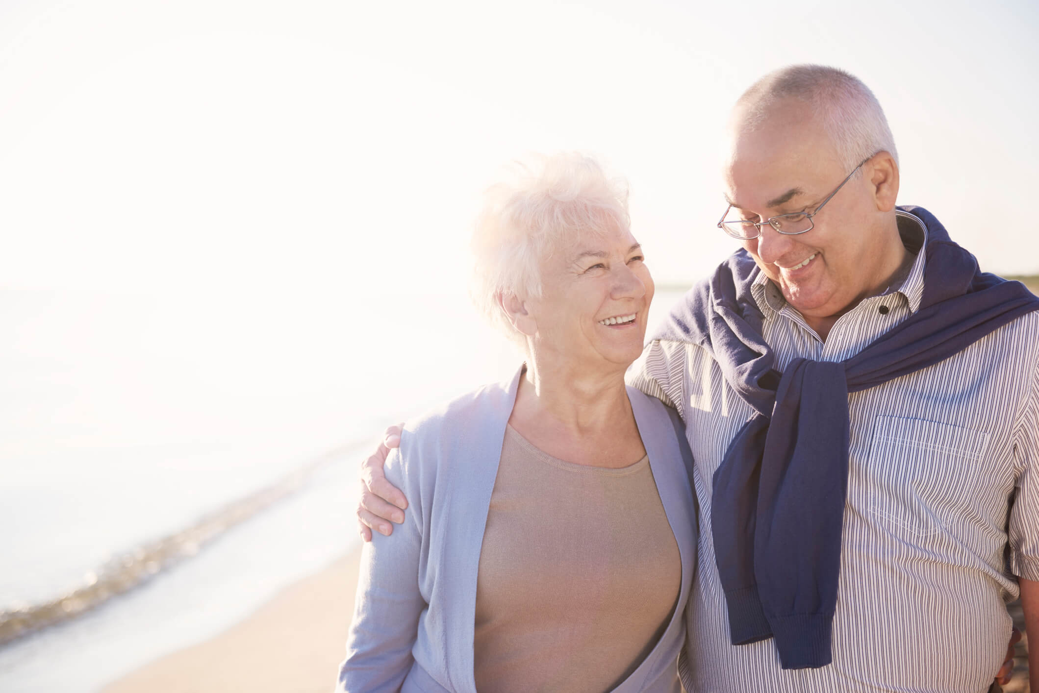 A smiling couple walks together along a sun-drenched shoreline, capturing the vibrant, active lifestyle near senior living near beaches in Clearwater, FL.