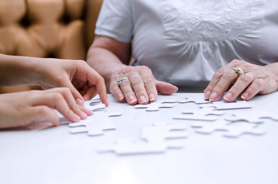 Two sets of hands gently work together on a white puzzle at a memory care community in Fort Myers, FL, a calming, engaging activity that supports connection and cognitive wellness for residents.