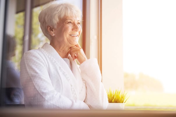 A resident smiles contentedly as she gazes out a sunlit window, capturing the peaceful and fulfilling lifestyle of independent living at Mirabelle, a welcoming senior community in South Miami, FL.