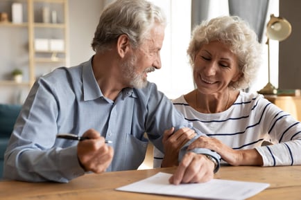 Two seniors sit together at a table, reviewing documents and sharing a smile, reflecting the ease of exploring senior living options in Mountainside, NJ with the guidance of a trusted community.