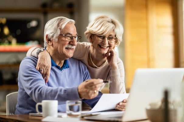 A cheerful older couple reviews a document together over coffee and a laptop, reflecting the everyday moments shared at senior living community Fulton MD and senior living near Elkridge MD.