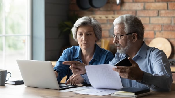 Two older adults sit together at a table reviewing documents and a laptop — researching and comparing assisted living vs. nursing home options near Bee Cave TX.