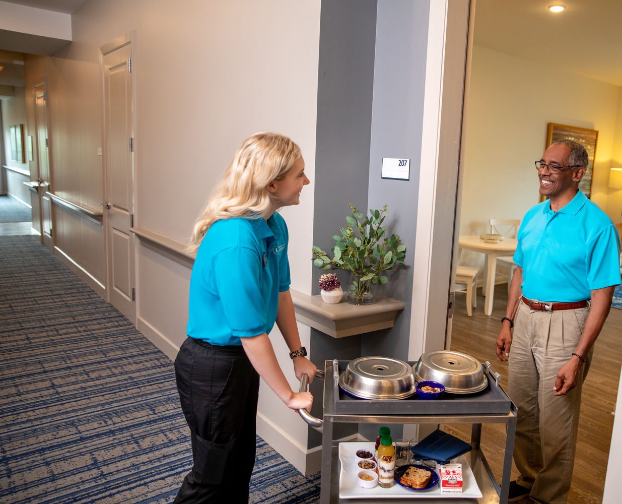 Team member and senior male chatting while breakfast is delivered