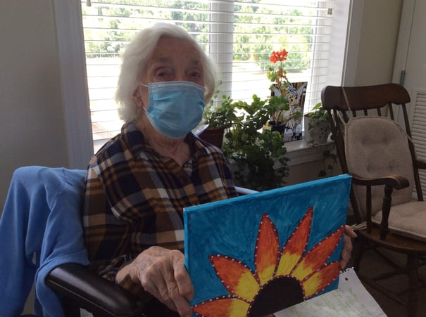 A resident proudly displays a vibrant painted canvas featuring a colorful flower, showcasing the enriching wellness activities at a memory care community in Suwanee, GA.