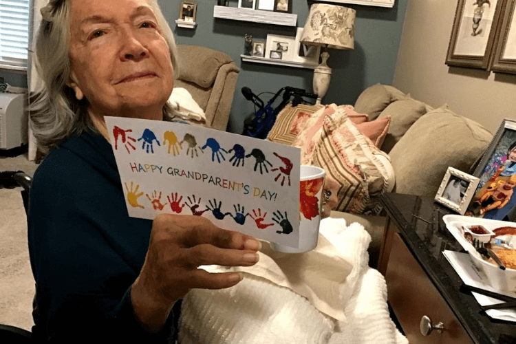 An older adult holds up a colorful handprint card reading 