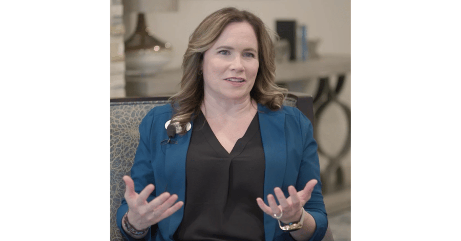 A woman in a blue blazer speaks expressively in a warmly furnished room — sharing expert guidance on dementia care Lakeway TX and how to help loved ones cope and thrive.
