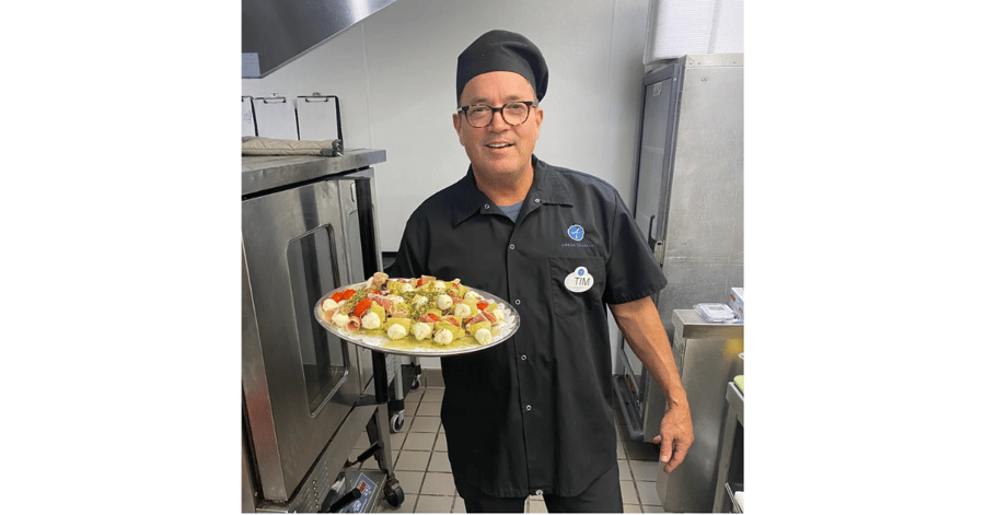 A smiling staff member in a chef's uniform holds a platter of freshly prepared appetizers in the kitchen — fresh, chef-crafted dining at senior living Lakeway Texas.