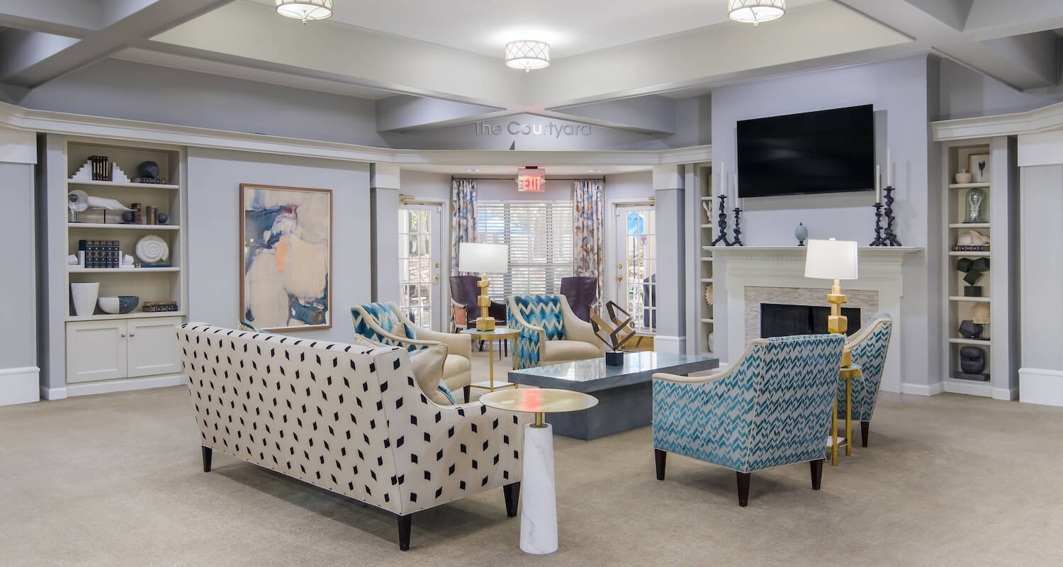 Arbor Terrace Decatur common area with a white and black polka dot couch and four blue chairs surrounding a coffee table. the couches are facing a tv and fireplace. artwork on the walls and windows 