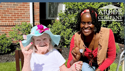 A resident wearing a colorful sun hat and a staff member share a joyful moment outdoors at Arbor Terrace Morris Plains, capturing the vibrant, personalized assisted living community spirit in Morris Plains, NJ.