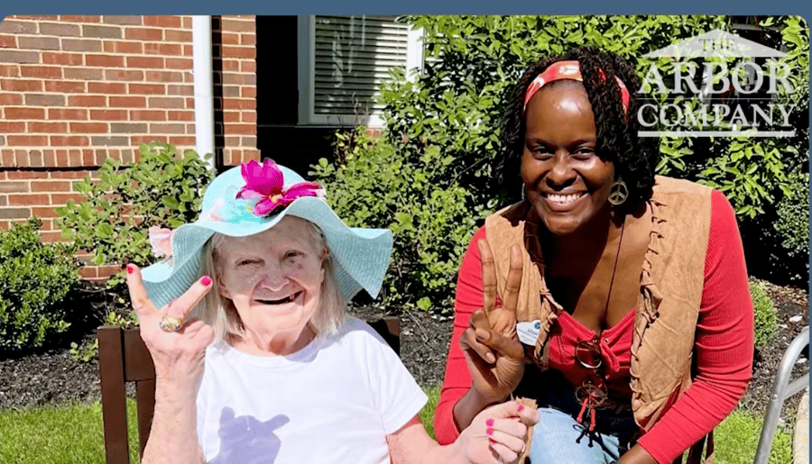 A resident wearing a colorful sun hat and a staff member share a joyful moment outdoors at Arbor Terrace Morris Plains, capturing the vibrant, personalized assisted living community spirit in Morris Plains, NJ.