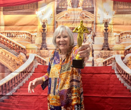 Una residente sonriente sostiene un trofeo dorado frente a un telón rojo con decorado teatral, reflejo de la vida sénior con actividades sociales en South Miami.