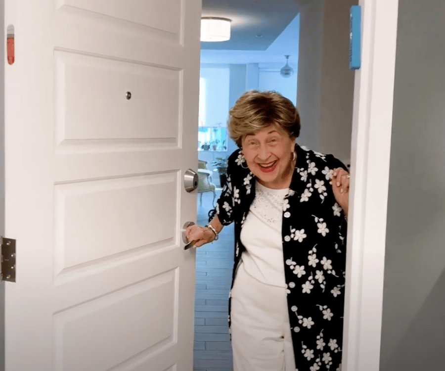 A resident beams with joy while opening the door to her apartment at Mirabelle, a warm and welcoming senior living community in South Miami, FL where every day feels bright and full of possibility.