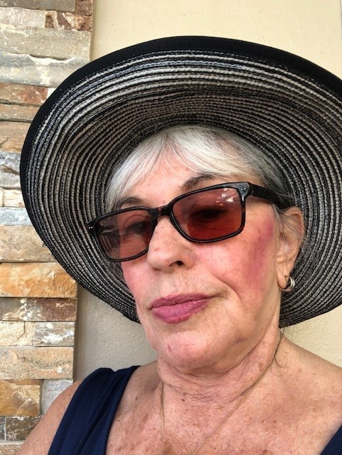 A confident resident poses outdoors in a wide-brimmed striped hat and tinted sunglasses, capturing the vibrant, independent spirit of senior living at Mirabelle in South Miami, FL.