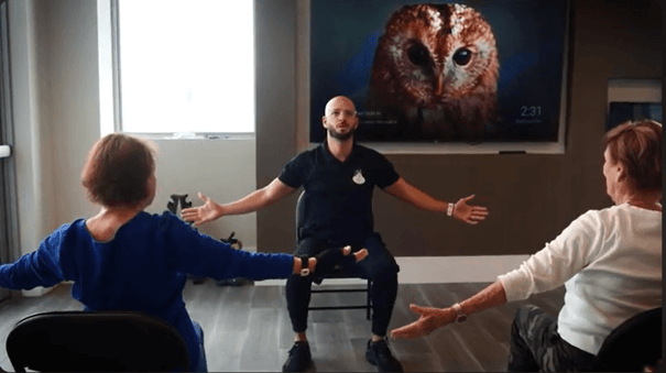 A fitness instructor leads two residents through a seated stretching class at Mirabelle, a vibrant senior living community in Miami, FL where engaging wellness programs support residents body and mind.