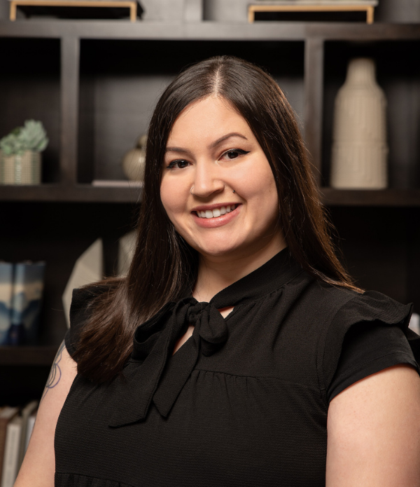 Miranda DeJesus, Business Office Director at Arbor Terrace Highland Park, smiles in a black tie-neck blouse in front of bookshelves, part of the friendly team behind senior living Highland Park IL and senior care Highland Park Illinois.