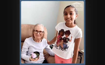 A resident holding a small flowering plant smiles warmly alongside a young visitor at Arbor Terrace Morris Plains, reflecting the heartfelt, family-centered senior living community in Morris Plains, NJ.