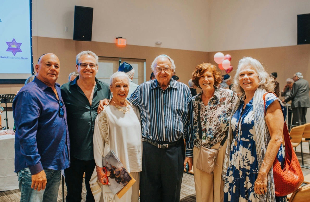 A group gathers together at a festive celebration with balloons in the background, sharing connection and community as part of senior living at The Arbor Company.