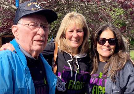 A resident and two supporters smile together outdoors at an Alzheimer's Walk event, reflecting the compassionate Alzheimer's and dementia care advocacy at Arbor Terrace Morris Plains, NJ.