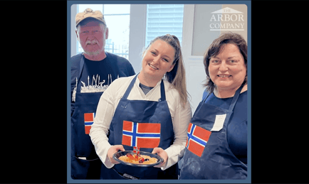 two seniors and a staff member wearing aprons with a Norwegian flag while presenting their food 