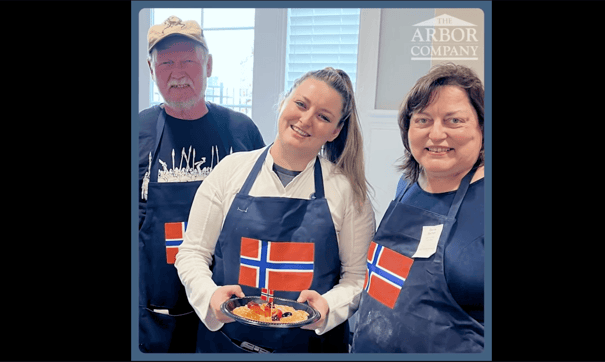 two seniors and a staff member wearing aprons with a Norwegian flag while presenting their food 