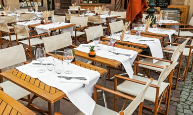 An open-air restaurant patio with neatly set wooden tables, white linens, and canvas chairs, reflecting the walkable senior living Woodbridge VA lifestyle and easy dining access near this senior living near Potomac Mills community.