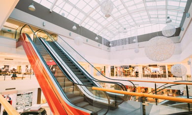 A bright shopping mall interior with sweeping red-striped escalators and skylights, showcasing the retail destination that makes senior living near Potomac Mills such a convenient part of life at senior living Woodbridge VA.