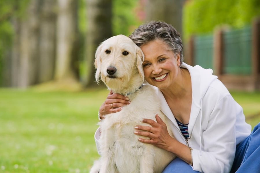 An older adult smiles and cuddles a fluffy golden dog outdoors in a grassy setting — celebrating the benefits of pet-friendly senior living Lakeway TX at Arbor Terrace.