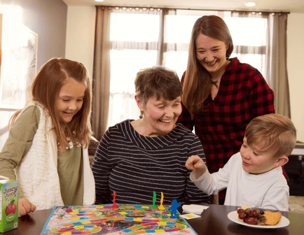 A senior woman smiles joyfully while playing a game with children and a younger adult, highlighting the warm intergenerational connections at this senior living community in Mountainside, New Jersey.