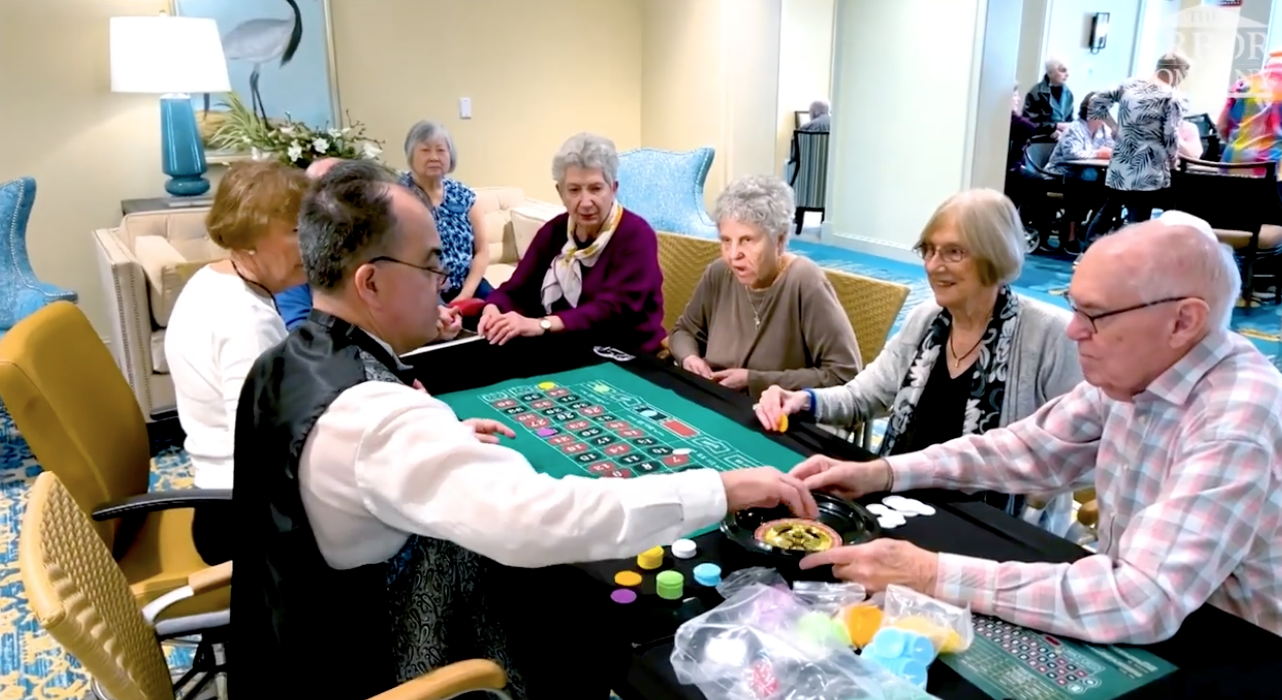 Residents gather around a lively casino-style table game with a dealer, capturing the fun, social activities at senior living in Citrus Park, FL.
