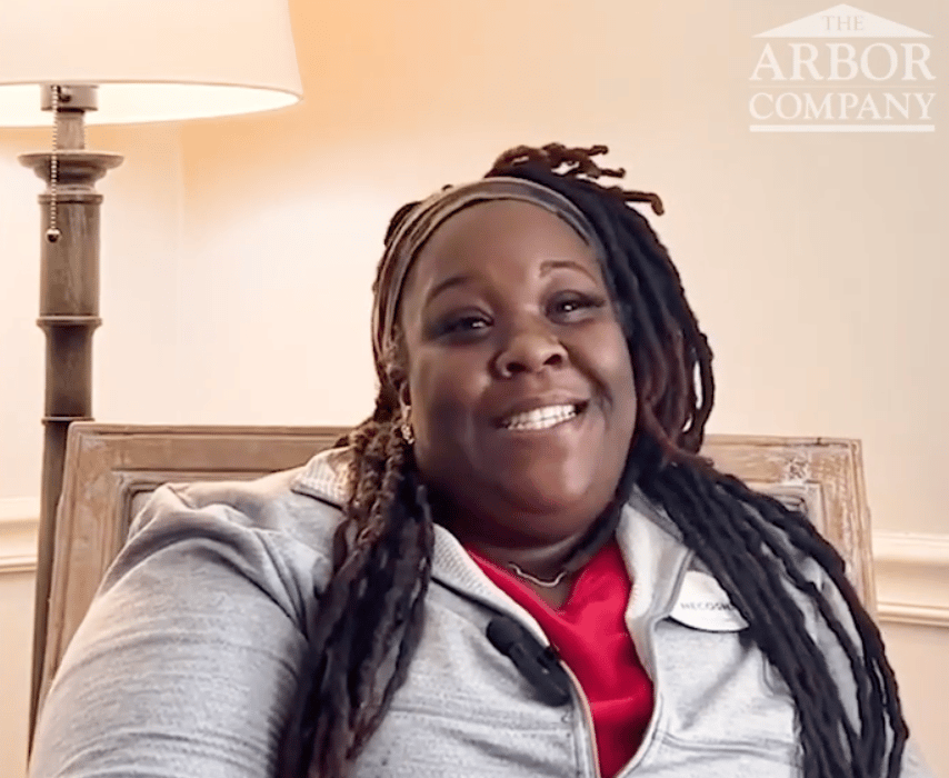 A smiling Arbor Terrace team member relaxes in a warmly lit room, reflecting the compassionate, heart-centered care offered at this senior living community in Athens, GA.