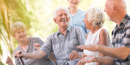 A lively group of seniors laughs and chats together outdoors in the sunshine, capturing the warm community spirit that defines senior living in Mountainside, NJ.