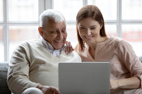 Two people smile together while looking at a laptop in a cozy, sunlit living space, exploring senior care options in Suwanee, Georgia.